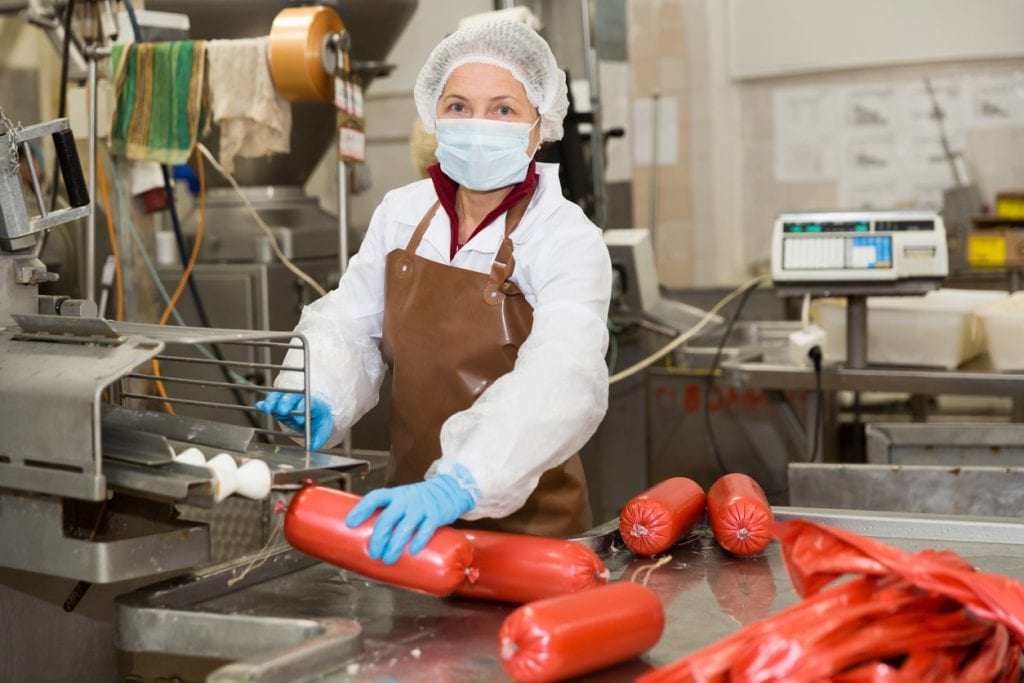 Female worker controlling conveyor of cooked sausages production on meat factory