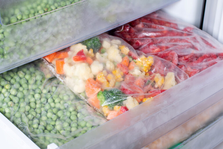 Plastic bags with different frozen vegetables in refrigerator.